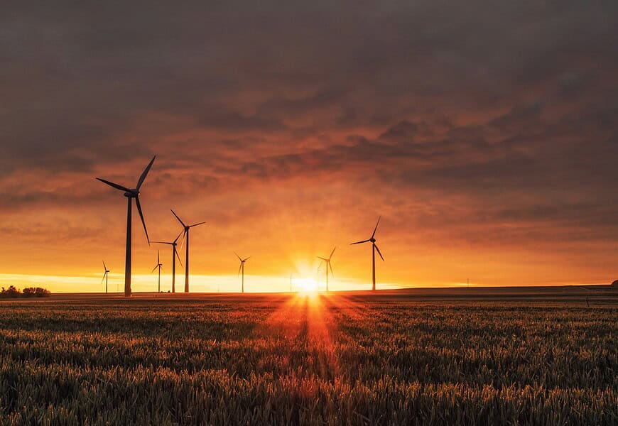 Parque eólico al atardecer con aerogeneradores en un campo de cereales, simbolizando la transición energética y la sostenibilidad
