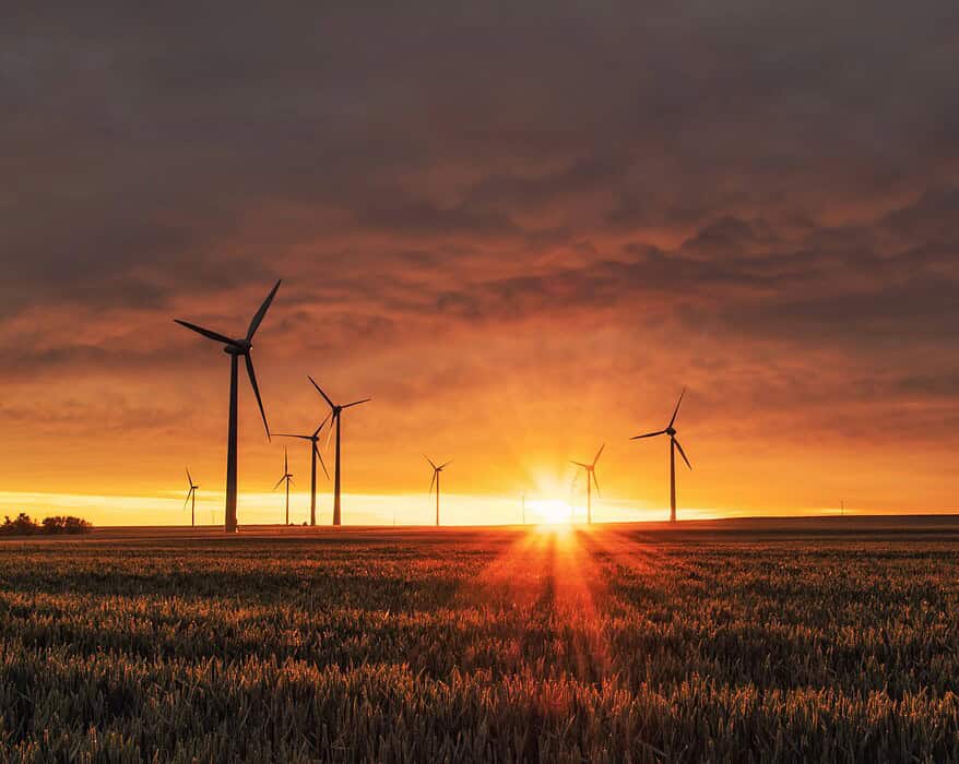 Parque eólico al atardecer con aerogeneradores en un campo de cereales, simbolizando la transición energética y la sostenibilidad