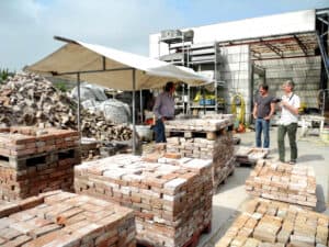 Trabajadores junto a palés de ladrillos reutilizados en una planta de reciclaje de materiales de construcción, ejemplo de ciclabilidad en la edificación