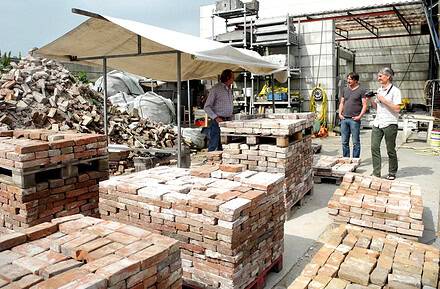 Trabajadores junto a palés de ladrillos reutilizados en una planta de reciclaje de materiales de construcción, ejemplo de ciclabilidad en la edificación