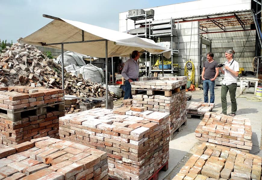 Trabajadores junto a palés de ladrillos reutilizados en una planta de reciclaje de materiales de construcción, ejemplo de ciclabilidad en la edificación