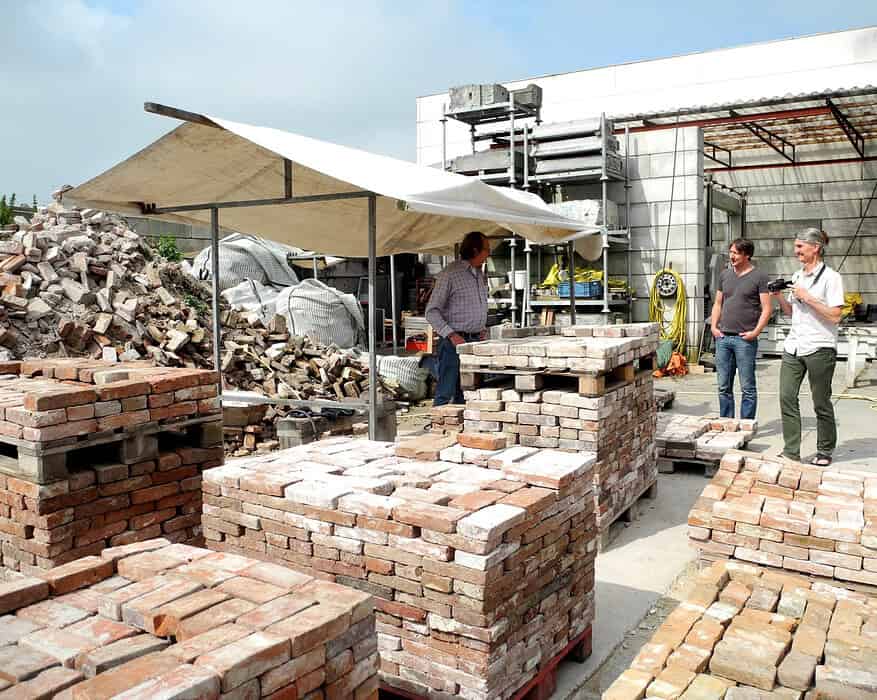 Trabajadores junto a palés de ladrillos reutilizados en una planta de reciclaje de materiales de construcción, ejemplo de ciclabilidad en la edificación